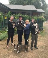 Four people and two dogs are standing in a dirt field.