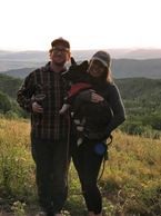 A man and woman holding a dog on top of a hill.