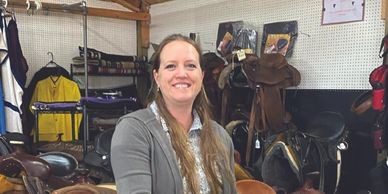 A woman standing in front of some horse saddles.