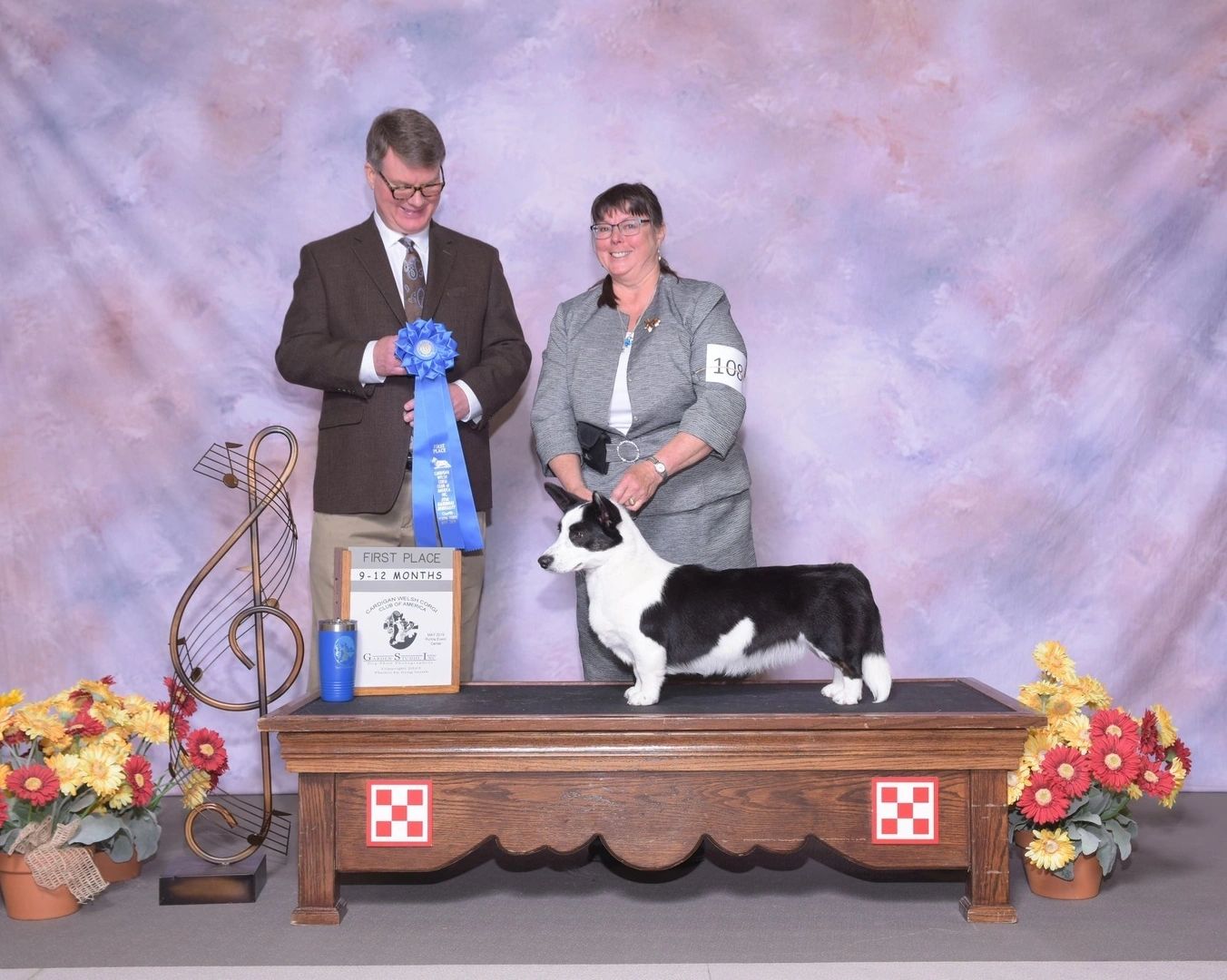 A man and woman holding a blue ribbon standing next to a dog.